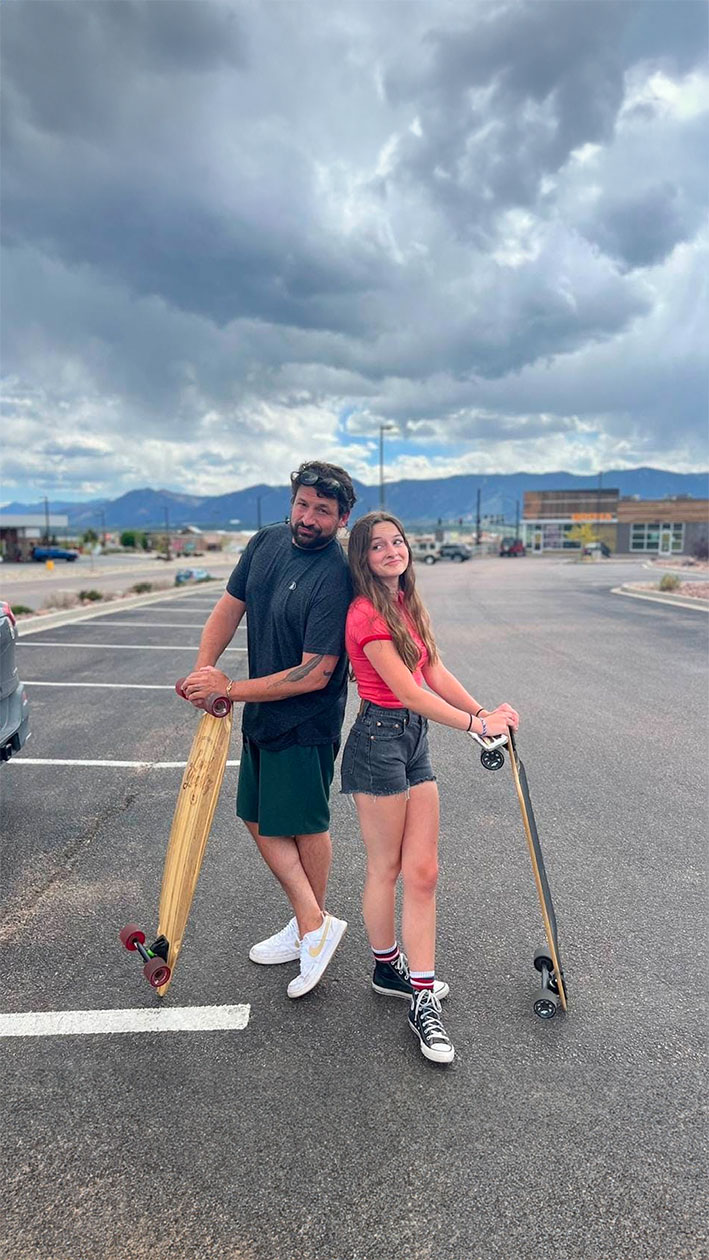 Father and daughter holding skateboards in a parking lot